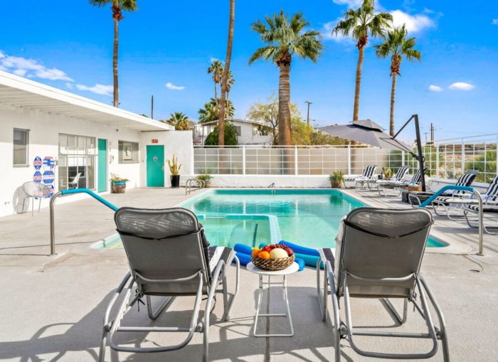 Sagewater spa swimming pool with the back of two pool-sie chairs in foreground palm trees and building in background