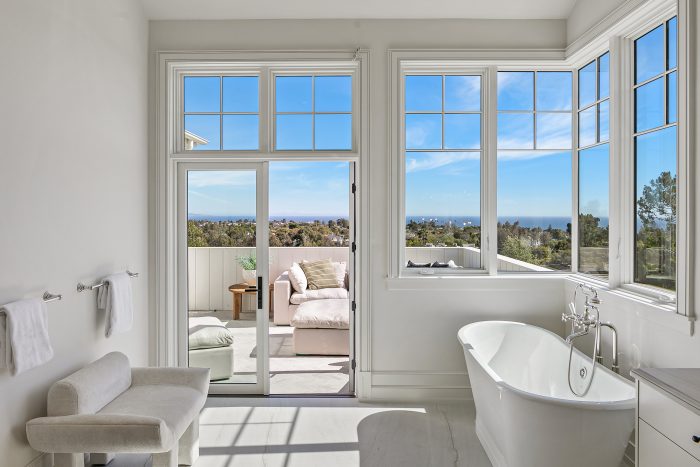 Bathroom with white tub, windows and doorway leading out to patio.