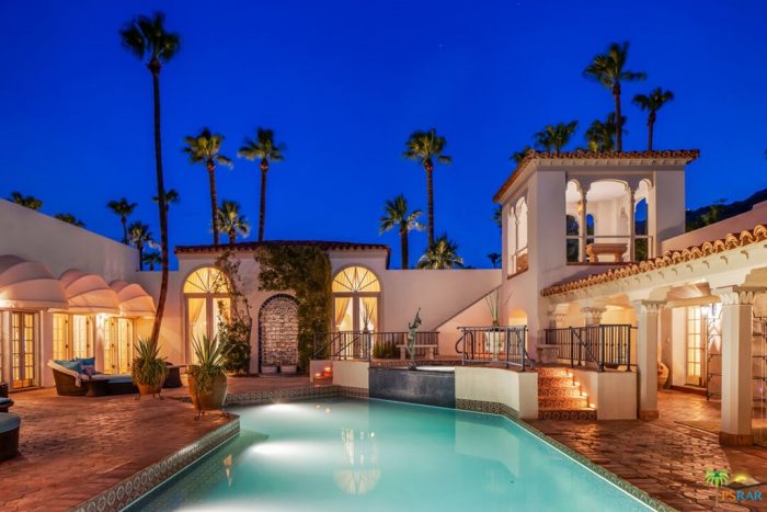 El Kantara Estate of Palm Springs after dark with swimming pool in foreground and palm trees behind Spanish Style estate