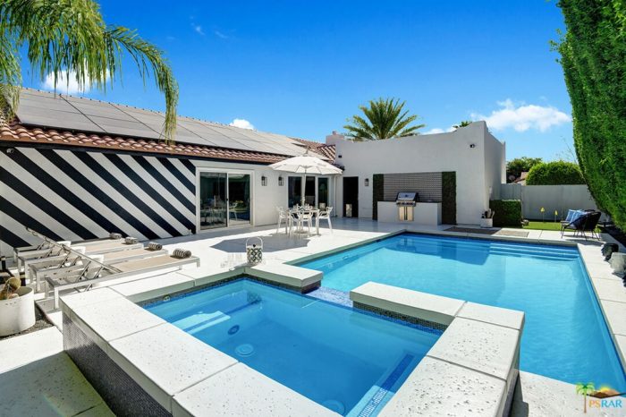 Square concerte modern design swimming pool with hot top in foreground and black white diagonal striped building in background