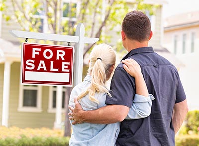 Couple standing in front of home for-sale sign