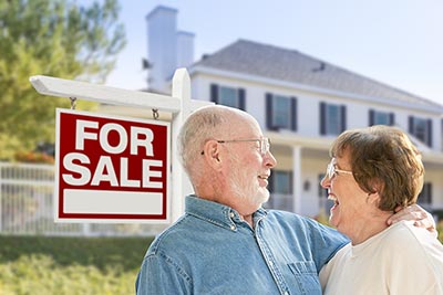 Older couple in front of home for-sale sign