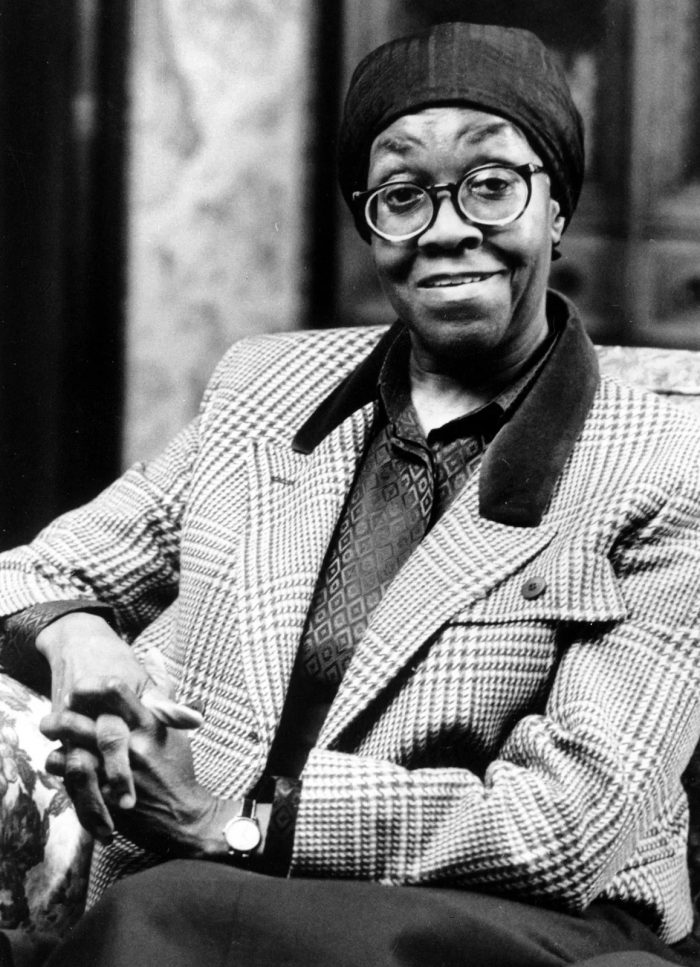 View of Gwendolyn Brooks sitting in a chair looking at the camera with hands folded in her lap