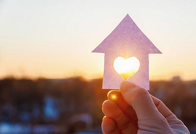 A hand holding a paper house with a heart cut in it