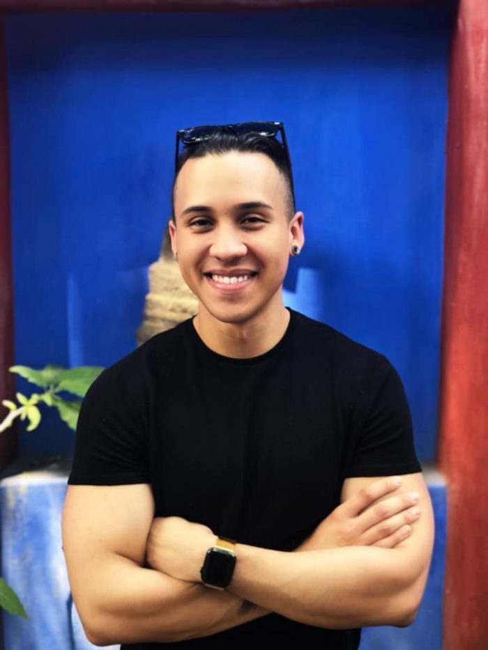 JD Thompson, Senior Associate, M&A Integrations - Young man in black shirt, in front of a blue wall
