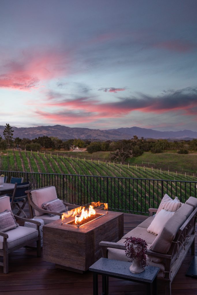 Outdoor fire place with furnishings and vineyard in background at dusk
