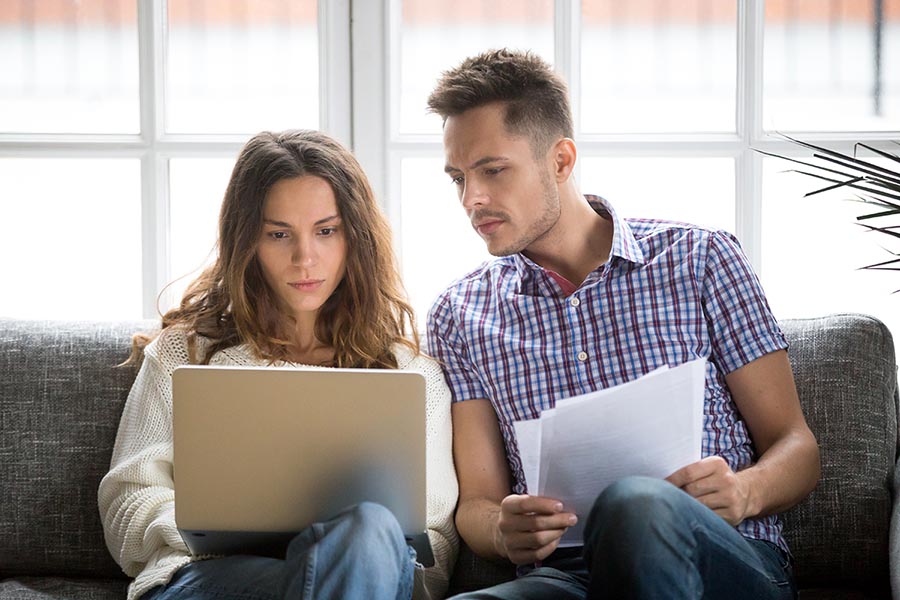 Focused worried couple paying bills online on laptop with documents