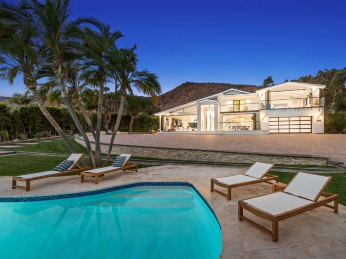 pool in foreground remodeled all white Malibu house in background with lights all on at dusk